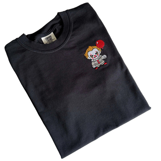 Folded black Comfort Colors T-shirt with a small embroidered Pennywise-inspired clown and red balloon on the left chest.