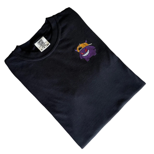 A folded black t-shirt with a small embroidered cartoon character on the left chest, laid flat on a white background.